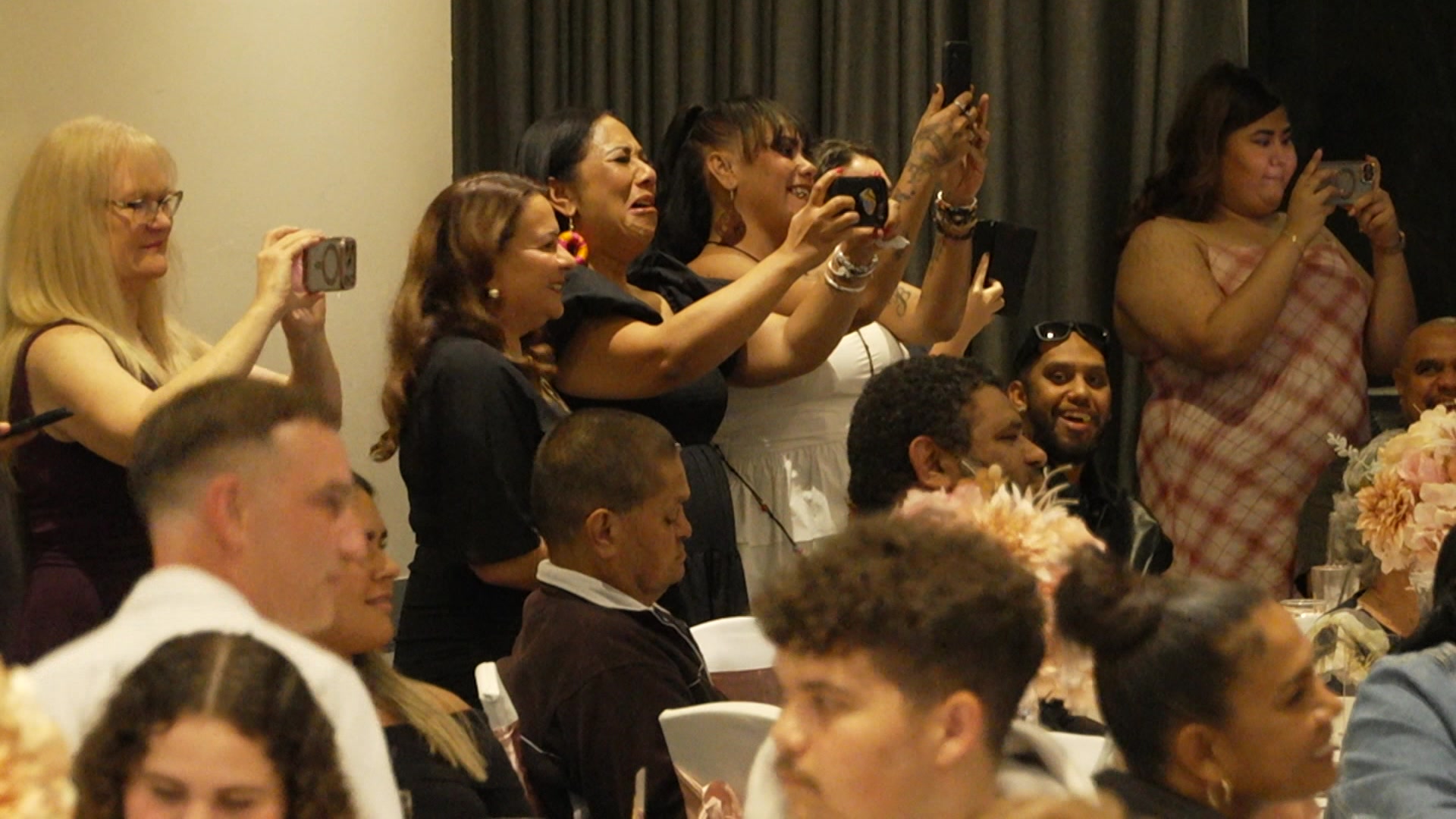 women in a crowd watching a dance routine, some are recording on their phones