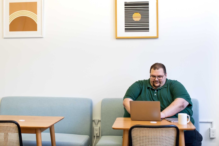 A large man in a green shirt sits by himself with a laptop in front of him
