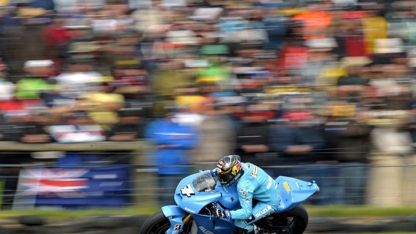 A man in a blue racing suit races a blue motorcycle around a track.