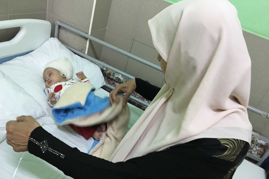 A Palestinian woman, Um Raed, stands over her three-month-old grandson Sajid, who has his head bandaged.