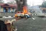 People look on as a car burns during a violent protest in Manokwari, Papua province, Indonesia.