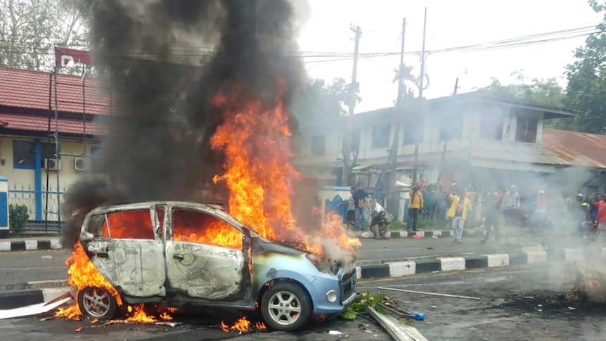 People look on as a car burns during a violent protest in Manokwari, Papua province, Indonesia.