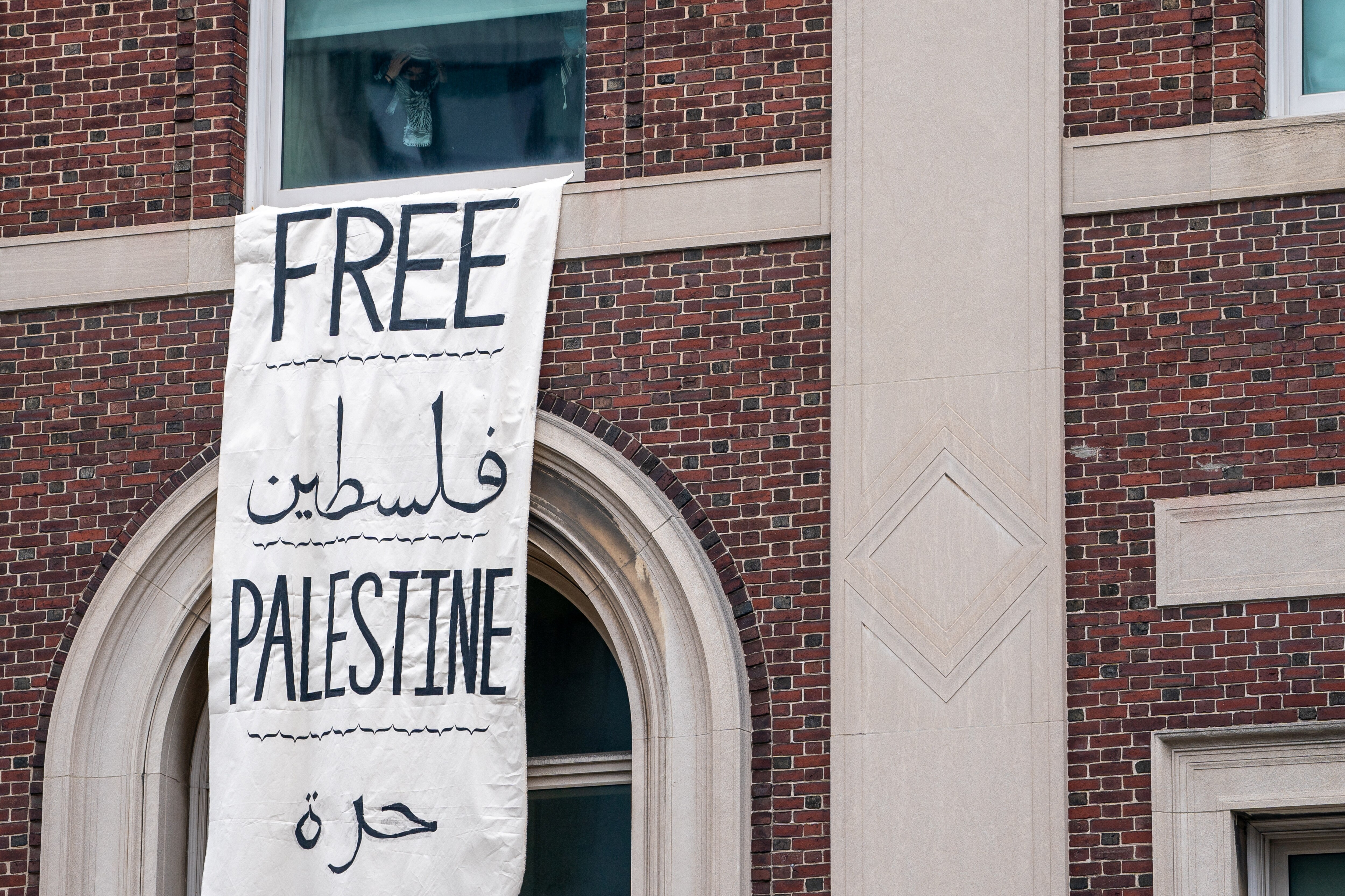 A large 'Free Palestine' banner hangs from a window of a brick building