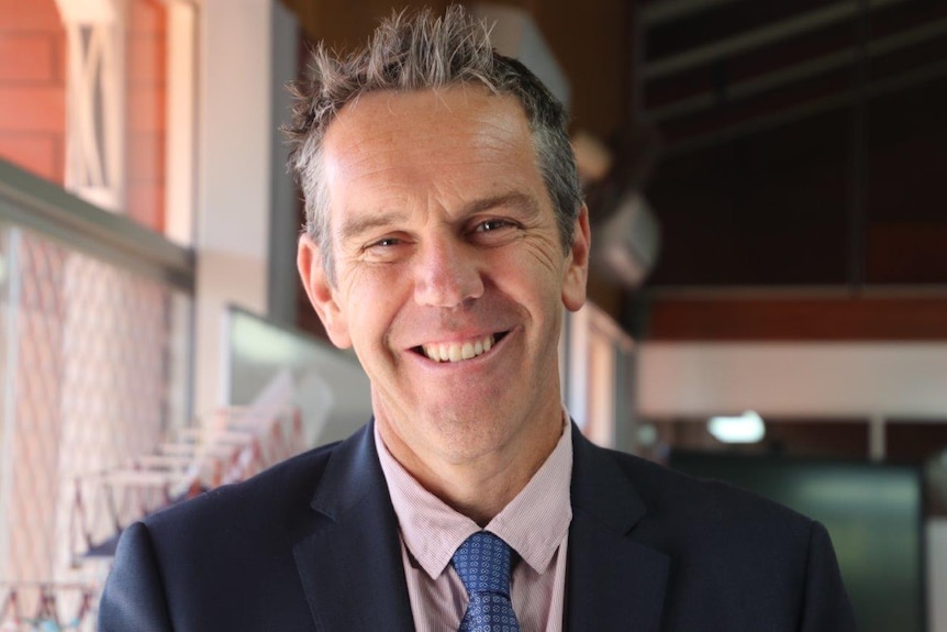 Anthony Middleton, wearing a suit standing inside a school building, facing the camera and smiling.