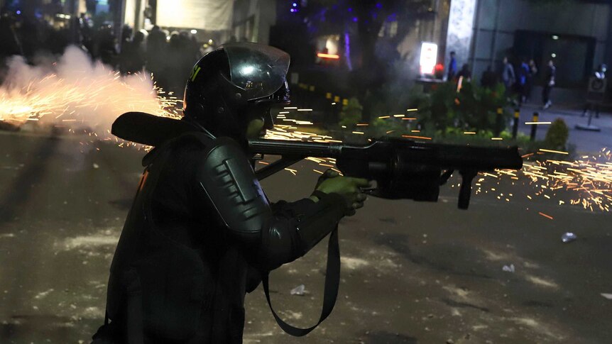 Sparks fly as an Indonesian police officer in riot gear fires a launcher during protests in Jakarta.