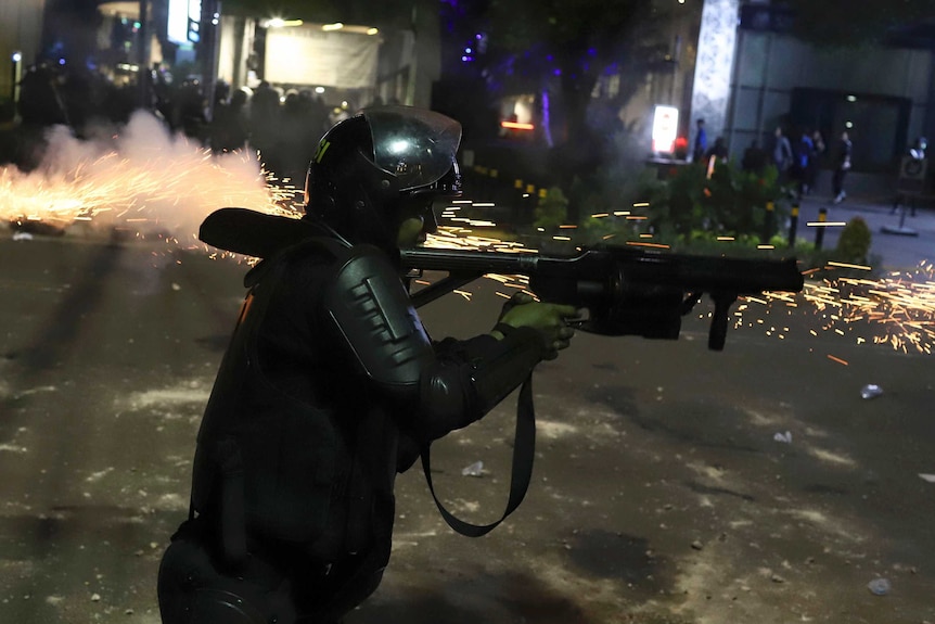 Sparks fly as an Indonesian police officer in riot gear fires a launcher during protests in Jakarta.