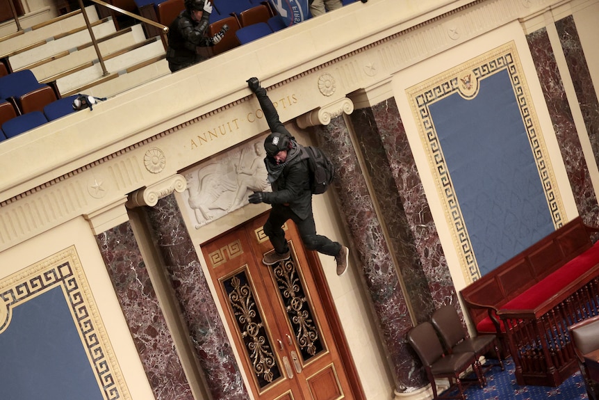 A man hangs from the balcony of the Senate Chamber in the US Capitol.