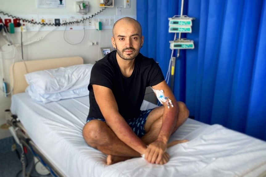 Angelo Romero in hospital sitting on a bed to received his first round of chemotherapy.