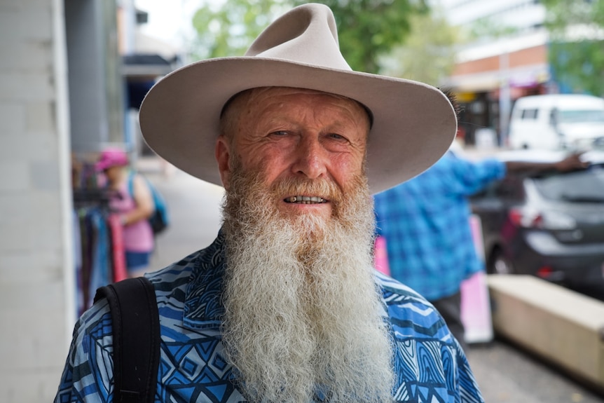 An older man wearing a hat standing outside smiling at the camera while wearing a wide-brimmed hat.