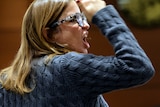 A woman raises her right arm and speaks with strong emotion inside a courtroom.