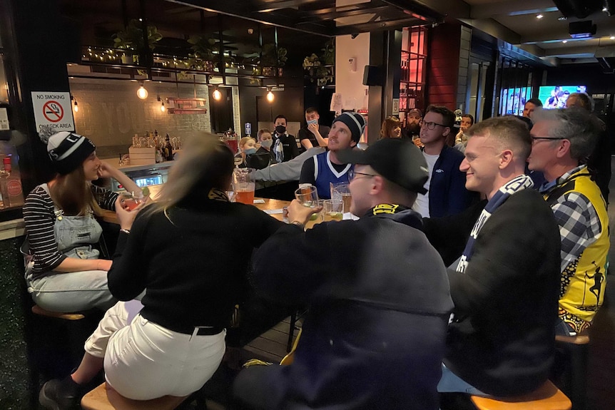 Geelong Cats fans smiling as they watch the AFL Grand Final at a pub.