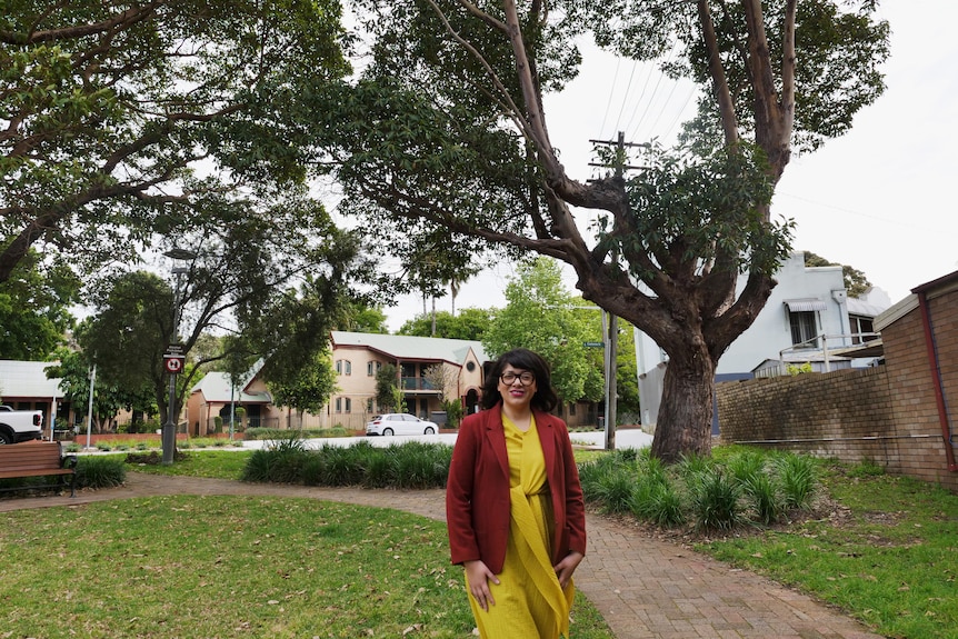 A woman stands under a tree with a power line running through it. 