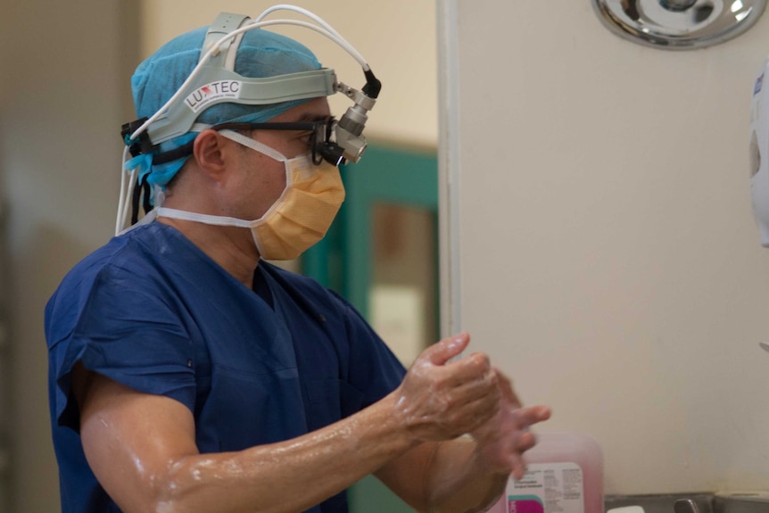 A side view of a surgeon in his hospital scrubs washing his hands