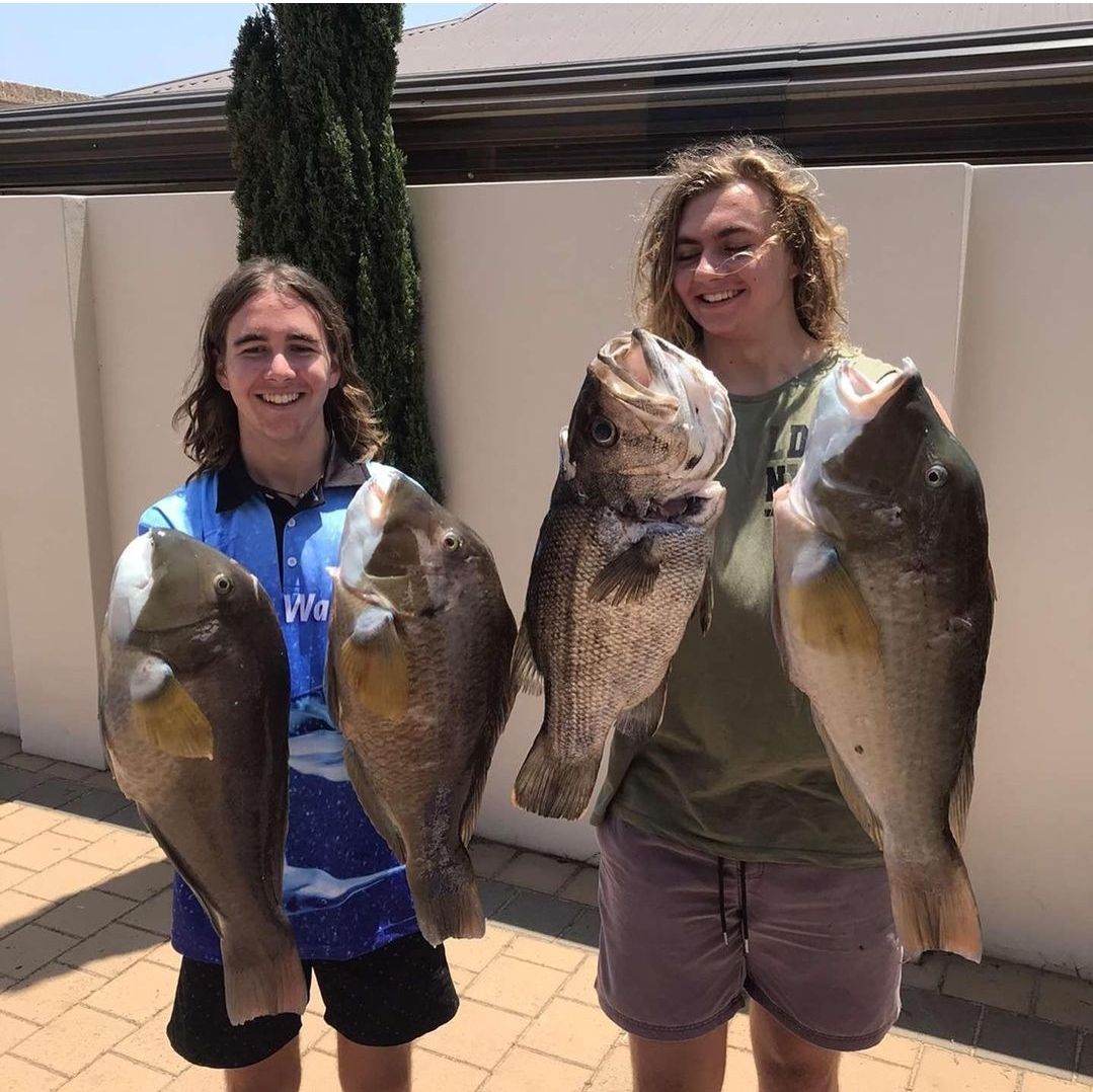 Two young men with long hair smiling holding big fish.