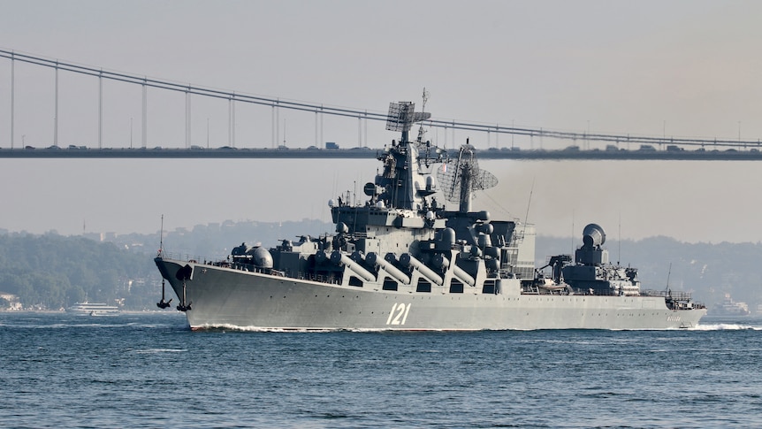 A large warship in water near a bridge. The numbers 121 are written on the side of the ship.