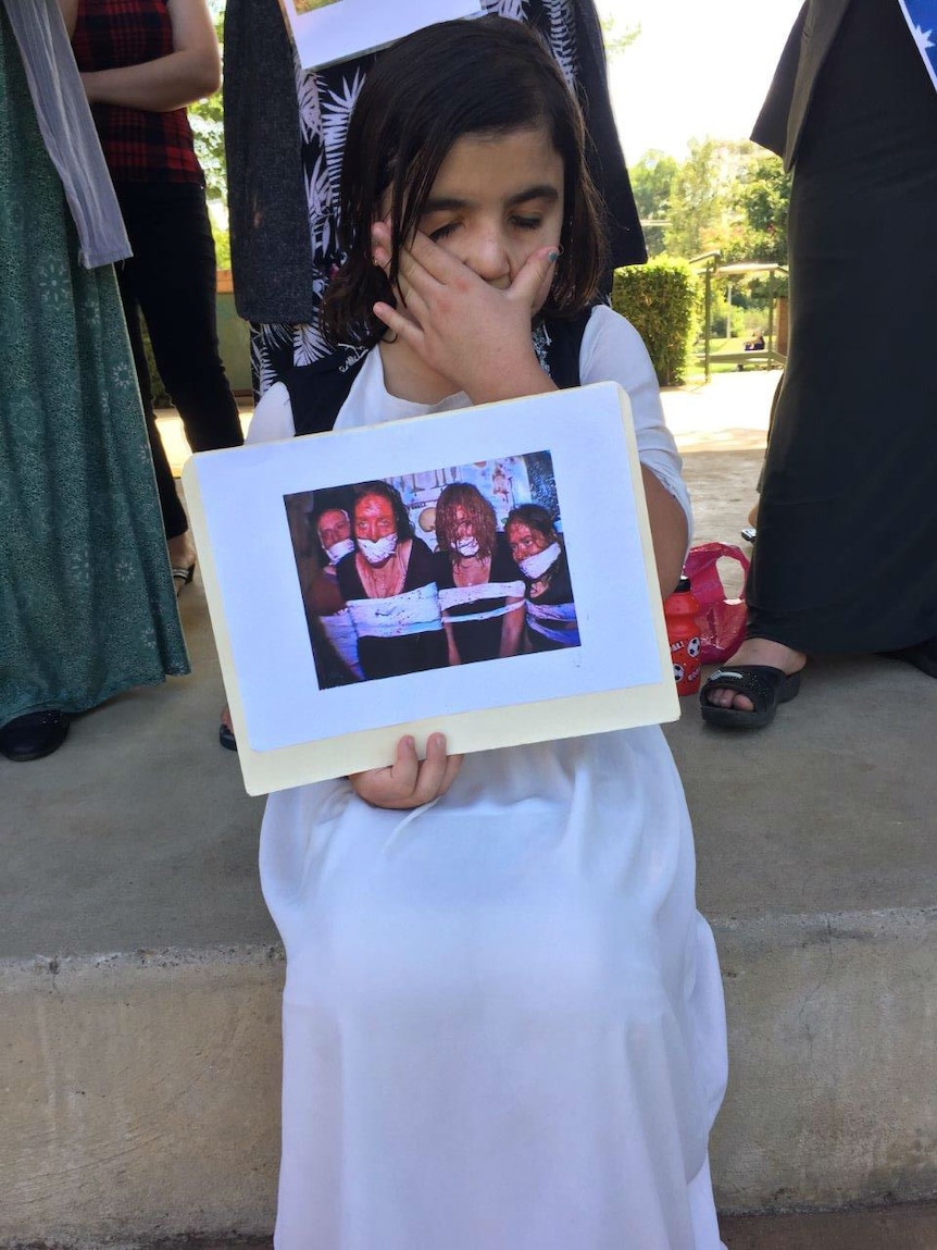 A young Yazidi refugee in Wagga holds up a photo of women captives at rally after latest massacre in Syria