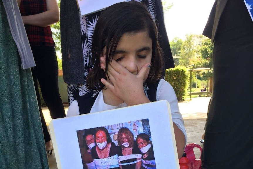 A young Yazidi refugee in Wagga holds up a photo of women captives at rally after latest massacre in Syria