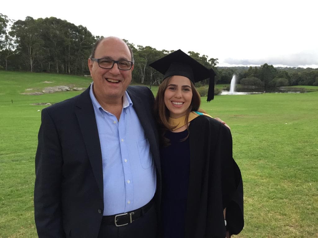 父と娘が草原で一緒に立ち、彼女の大学の卒業式で微笑みます。