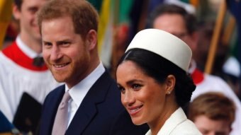 Prince Harry wears a suit, Meghan a white dress and white hat.