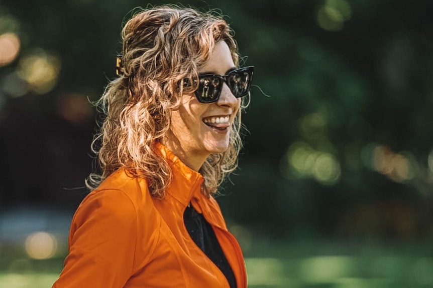 a woman in an orange jacket smiles and pokes her tongue out