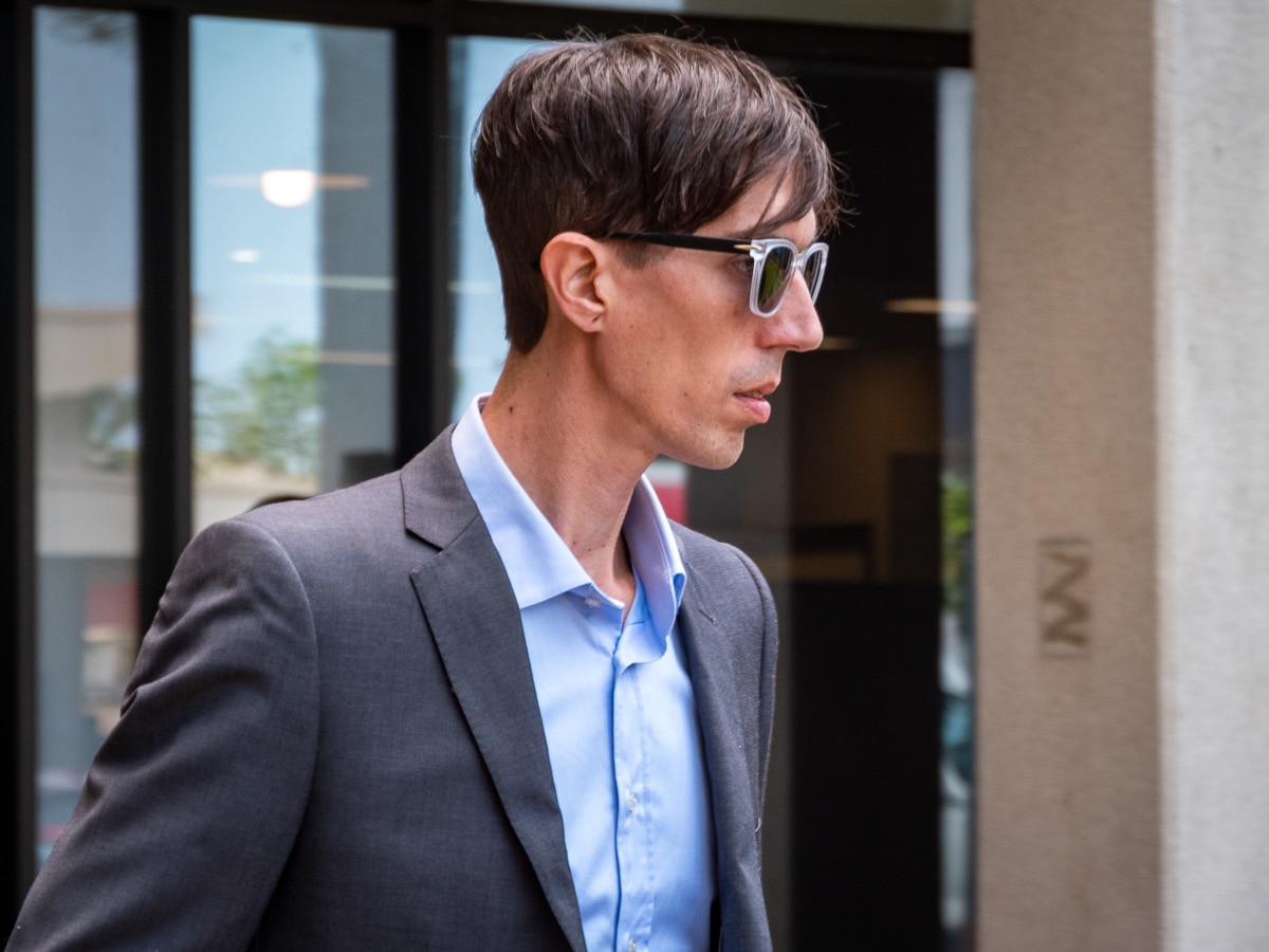 Homem de cabelos curtos e escuros, vestindo terno cinza, camisa azul e óculos escuros.