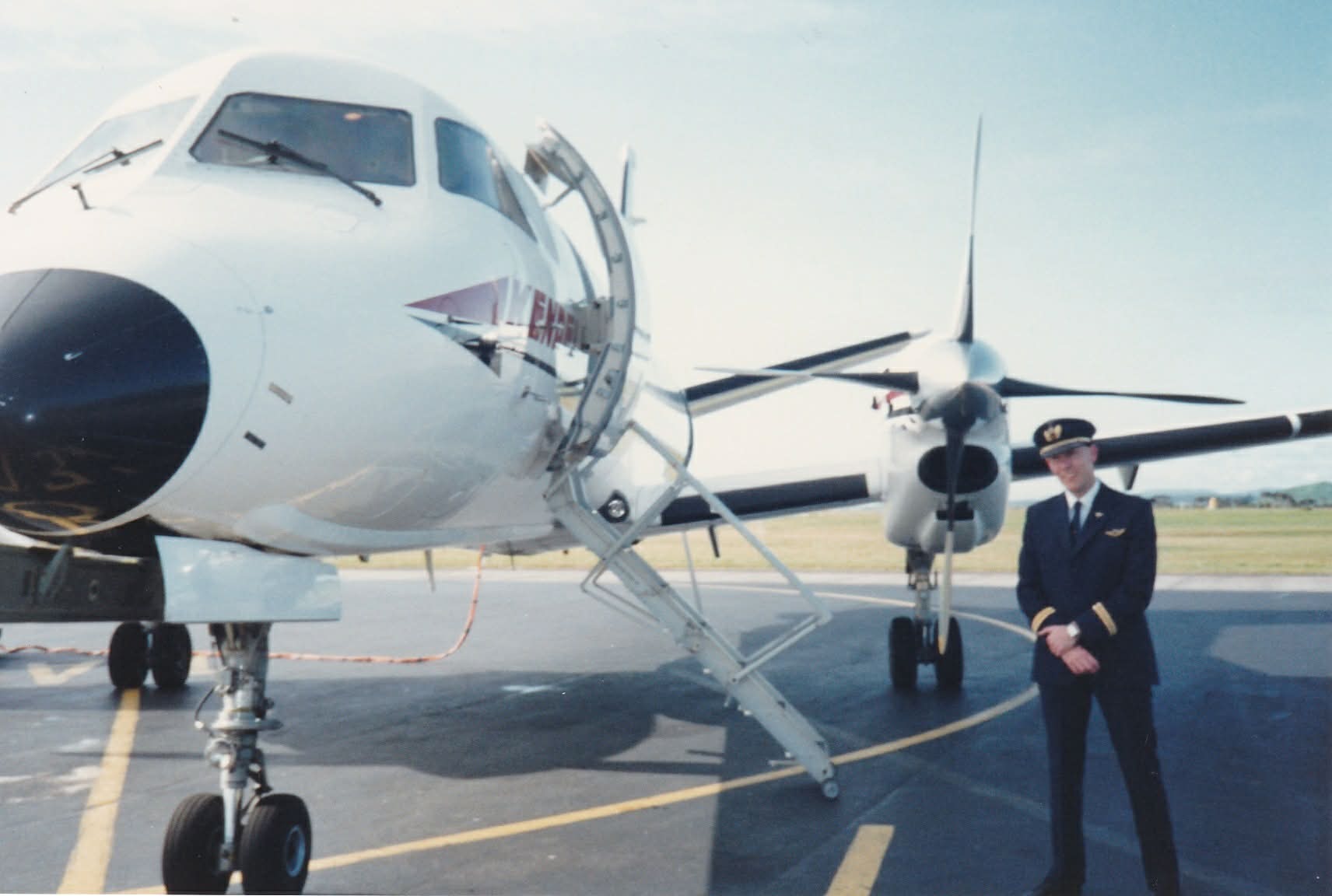 Mr Klouth in a pilot's uniform and hat standing in front of a plane wing on the tarmac.