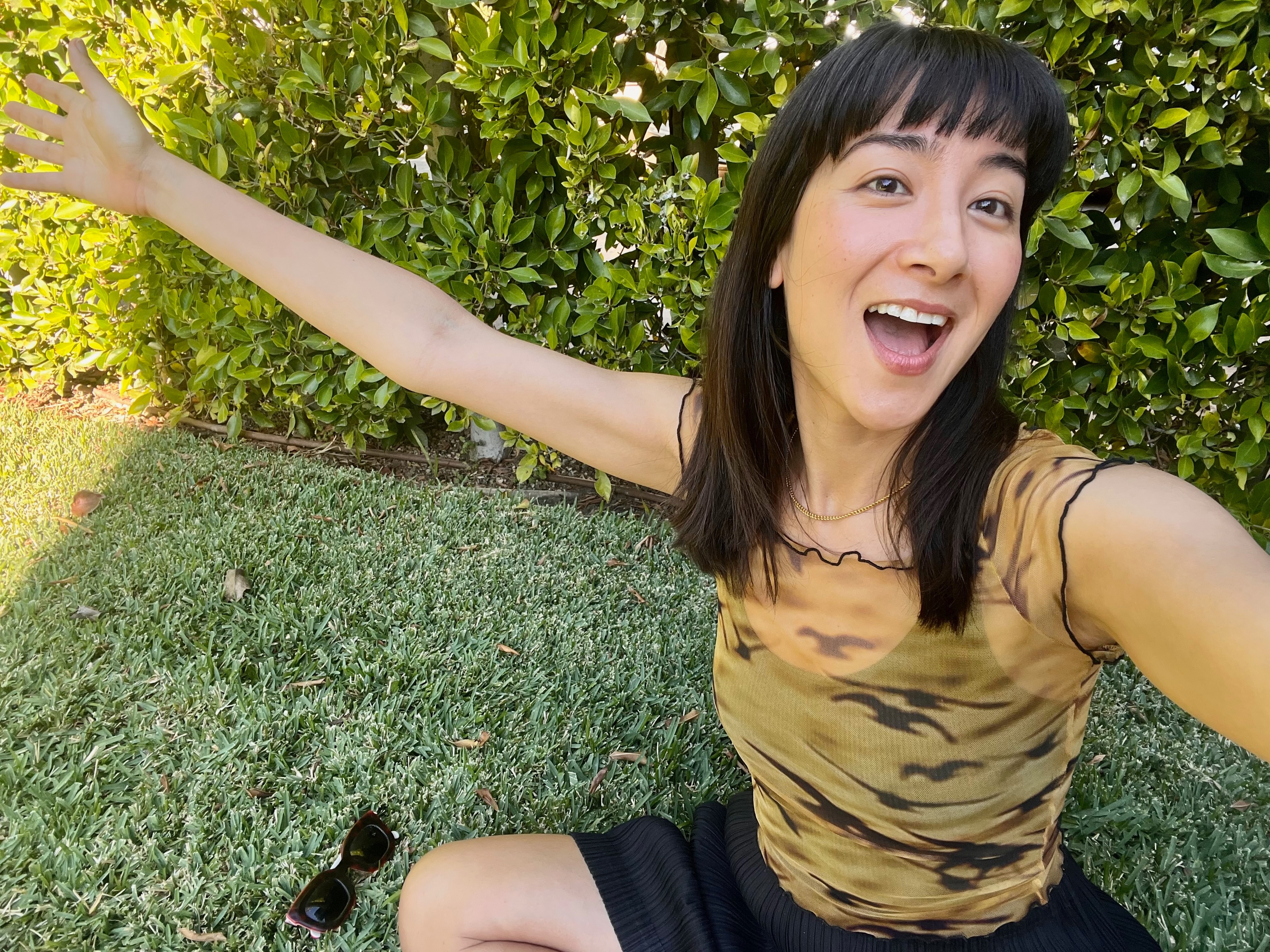 Podcaster, radio and TV host Linda Marigliano takes a selfie while sitting on the grass, smiling.