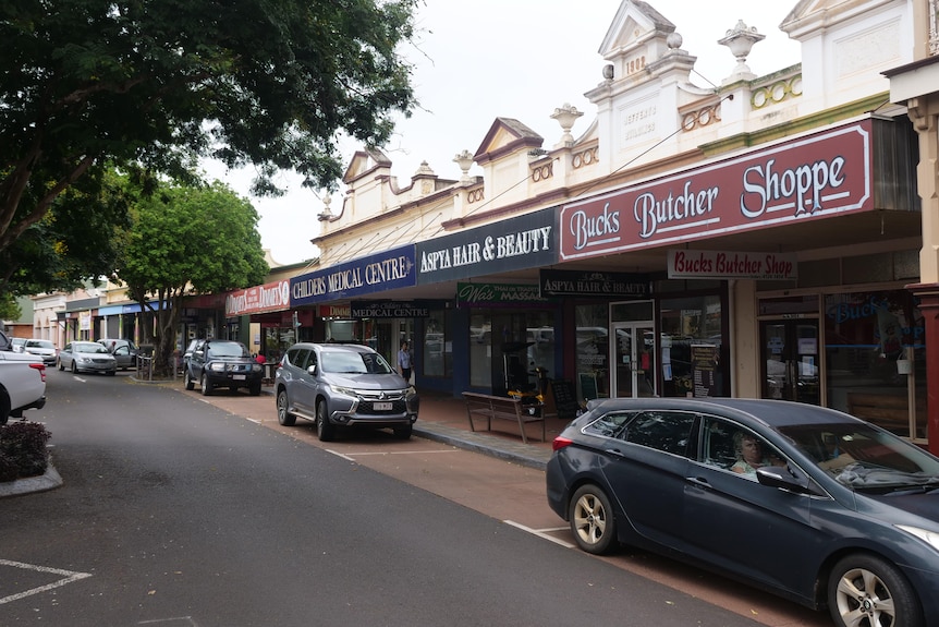 A series of shopfronts set in older buildings face the street with several cars in front. 