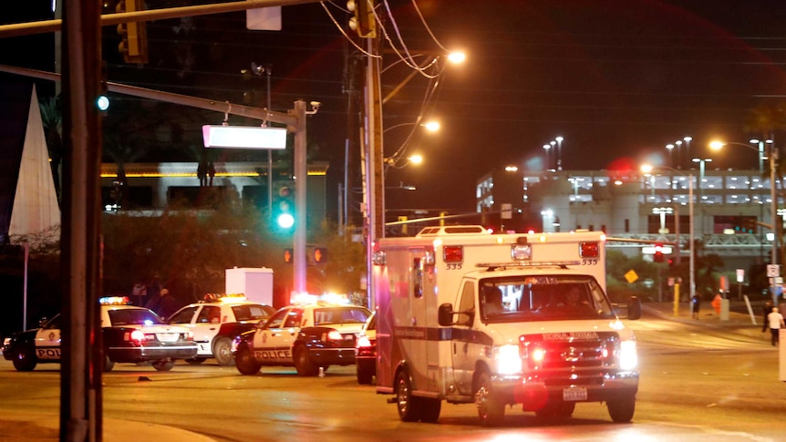 An ambulance and police cars with their emergency lights are on a street.