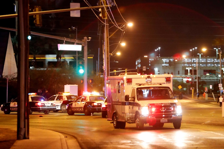 An ambulance and police cars with their emergency lights are on a street.