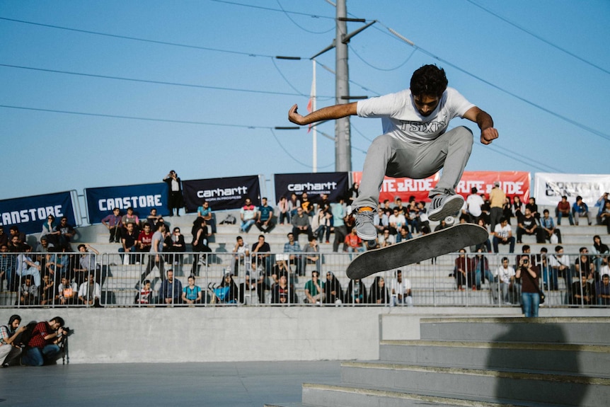 A skateboarder up in the air in the middle of a jump, wearing a TSIXTY shirt.