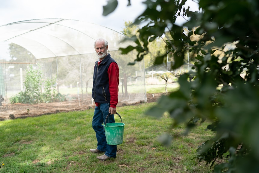 Man standing in his vegetable garden on his rural property looking at camera not smiling 