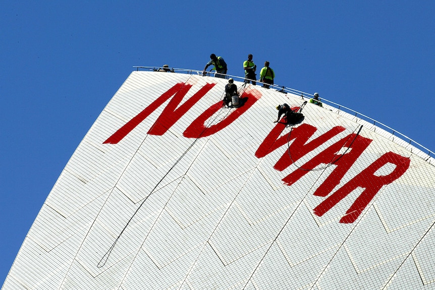 Close-up of men abseiling from top of Opera House sail and begin to paint over the red NO WAR letters with white paint