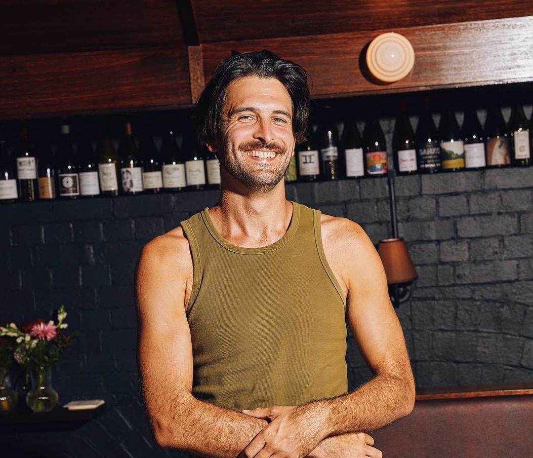 A man with brown hair smiling with his arms crossed wearing a green singlet. 