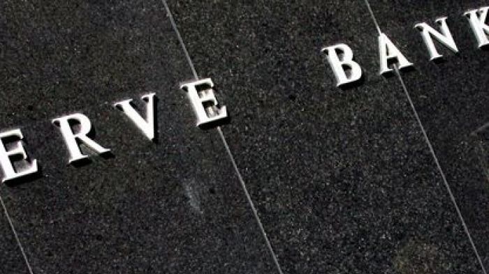 A white collar worker is reflected in the polished black granite facade of the Reserve Bank building in Sydney.