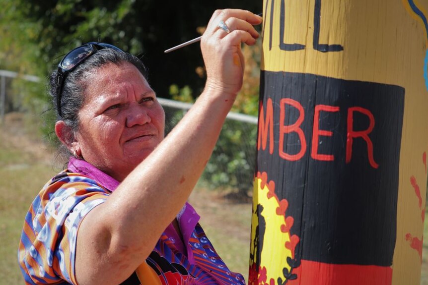 A woman using a paintbrush painting a wooden pole