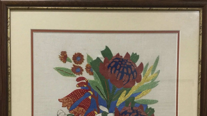 A framed embroidery featuring flowers and letters