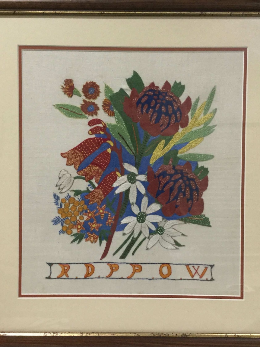 A framed embroidery featuring flowers and letters