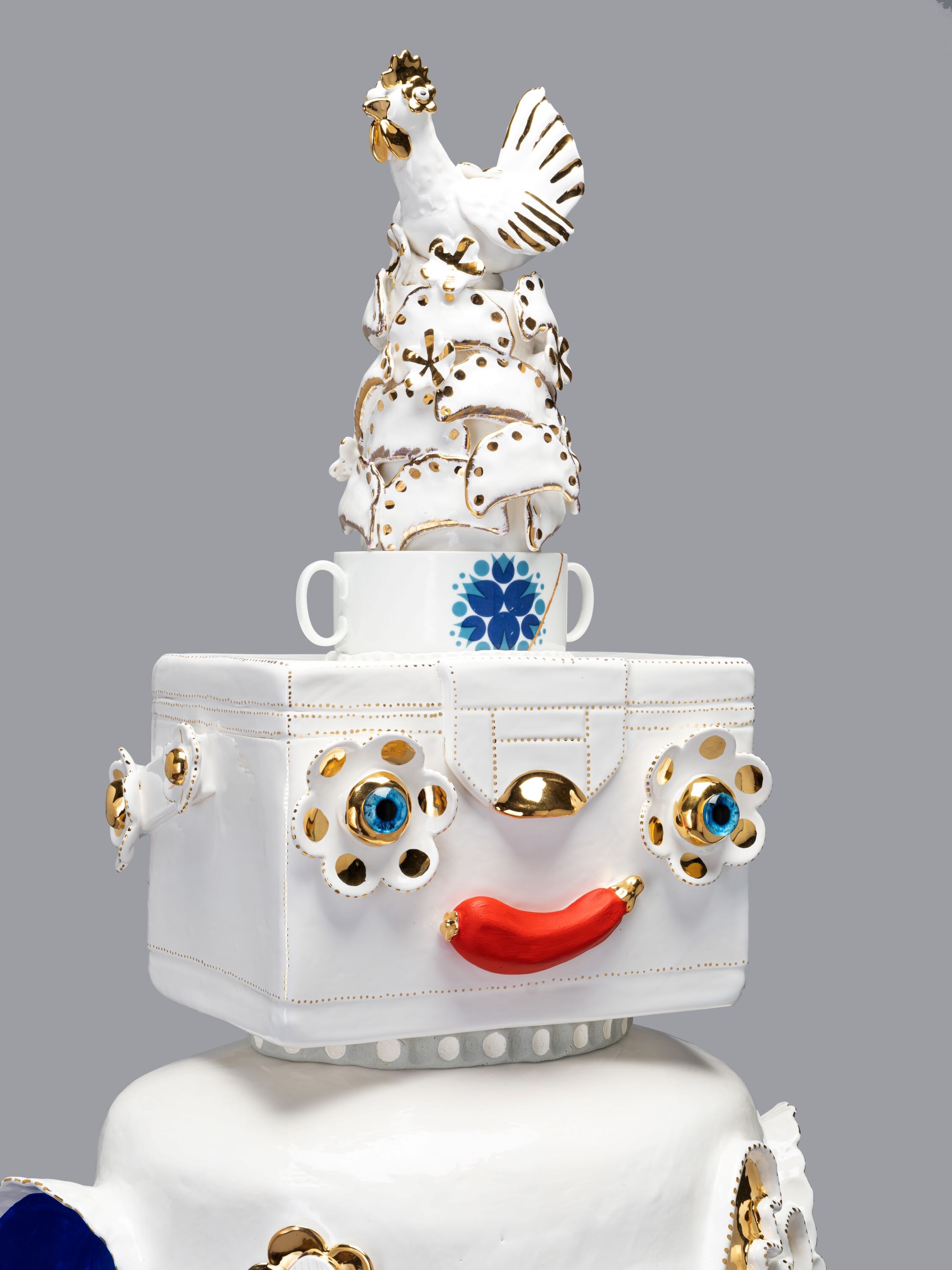 A white ceramic sculpture with an Esky-shaped head and a red chilli for lips, crowned with a rooster embossed in gold