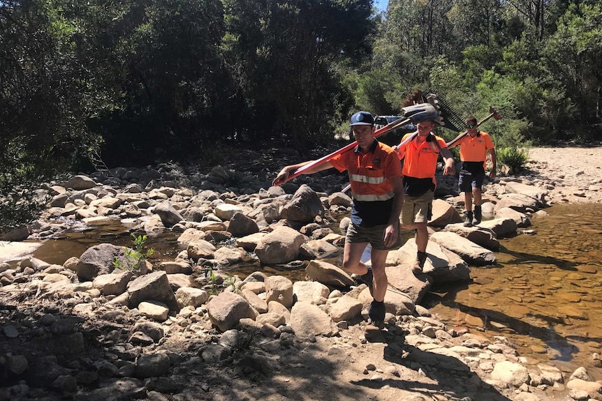 The Blue Derby trail maintenance crew cross a creek carrying shovels.