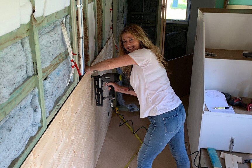She staples a board to a wall inside her tiny house