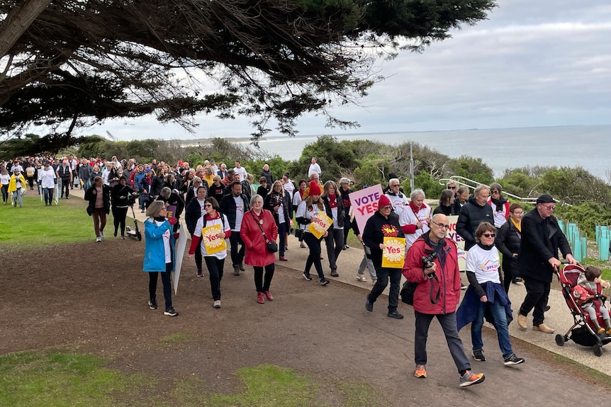 A crowd of people walk along a seaside path at Come Together For Yes in Torquay