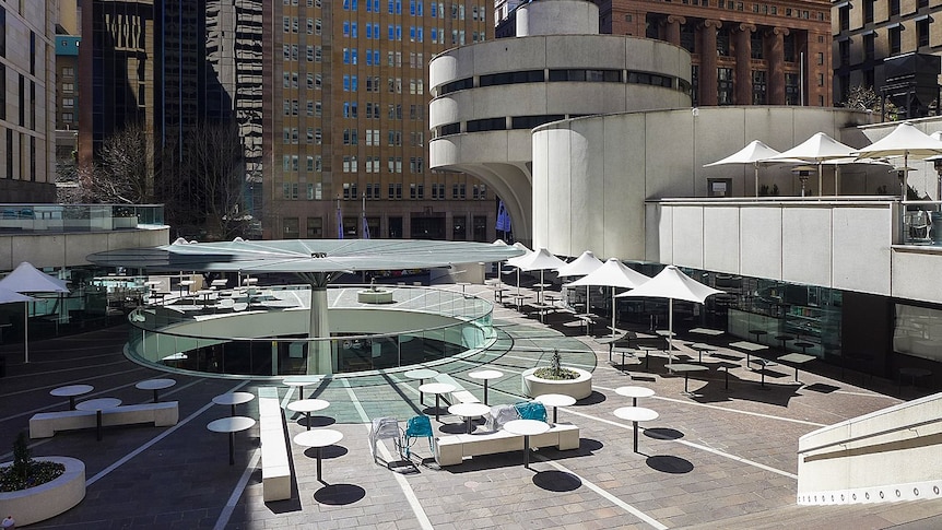 You look onto an empty raised plaza featuring fixed street furniture as you view Sydney's MLC Centre in the distance.