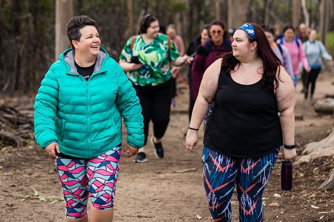 Two people smiling lead a group of walkers, wearing warm jackets and tights, with trees and forest landscape surrounding them.