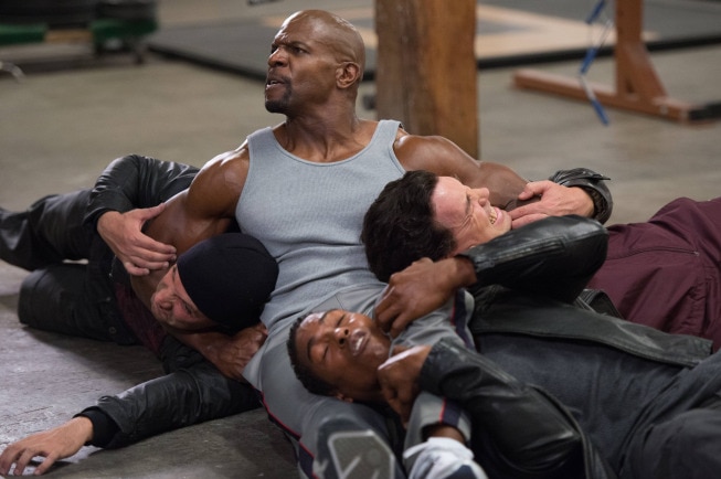 A muscular man holds three men in headlock.