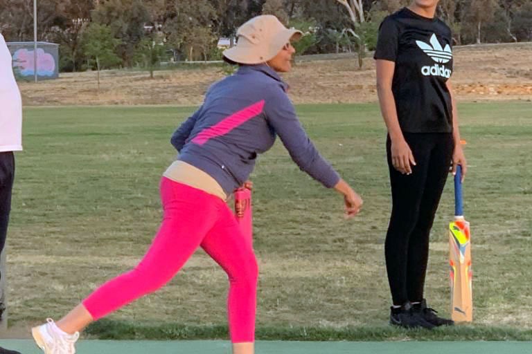 A woman in exercise gear learns to bowl a cricket ball.