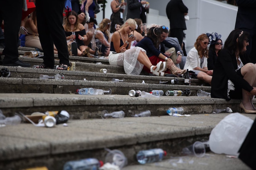 People sit on steps, surrounded by bottles, cans and plastic champagne bottles and cups.