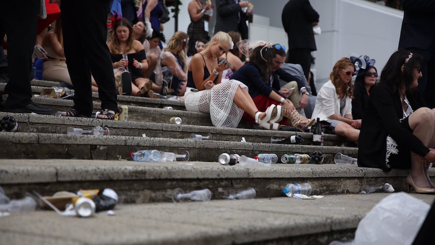 People sit on steps, surrounded by bottles, cans and plastic champagne bottles and cups.