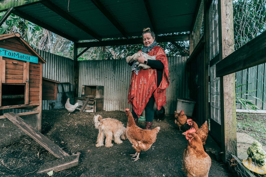 Ang Bennett holds a dog in a chicken pen