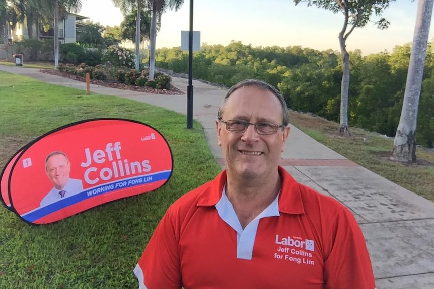 A man stands in a park in front of a political sign.